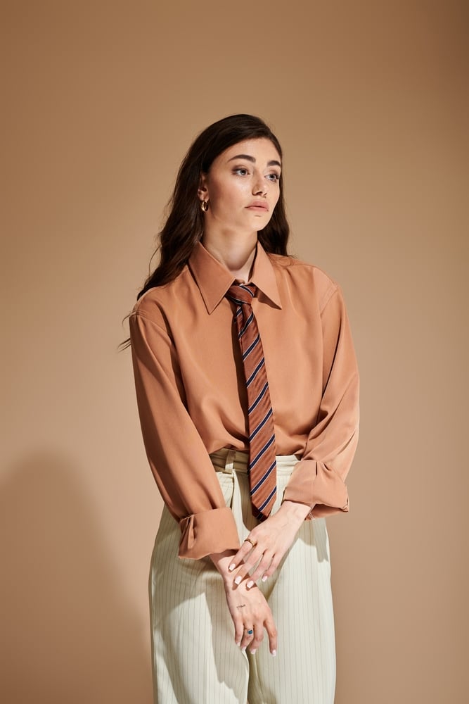 Style Professionnel Femme : Look Chemise Terracotta et Cravate Femme en chemise terracotta, cravate rayée et pantalon clair à rayures, style professionnel moderne et élégant.
