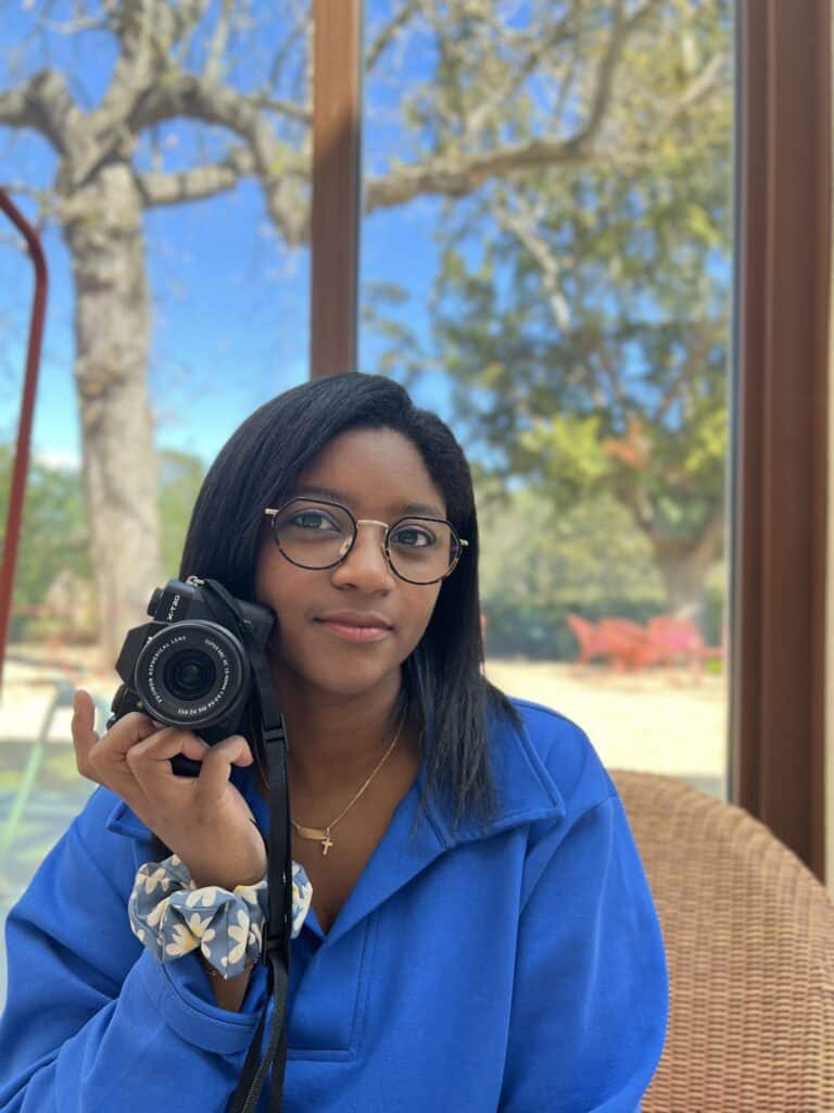 Photographe avec Fujifilm X-T20 et Objectif Fujinon Femme à lunettes tenant un appareil photo Fujifilm X-T20 et objectif Fujinon, vêtue d'un pull bleu éclatant.