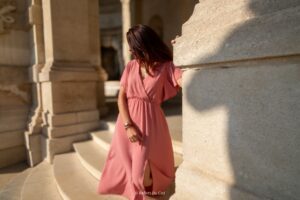 Femme en robe longue rose sur les marches d'un monument historique, ambiance douce et ensoleillée.
