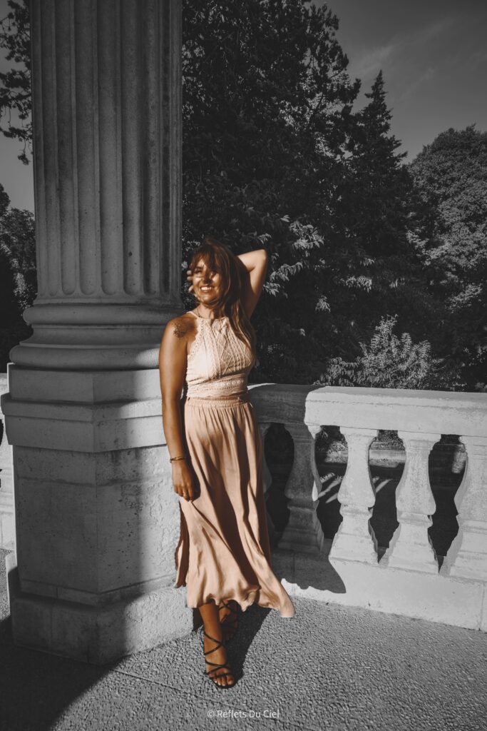 Shooting mode femme devant colonne classique - Reflets Du Ciel Femme souriante en tenue beige devant une colonne classique. © Reflets Du Ciel.